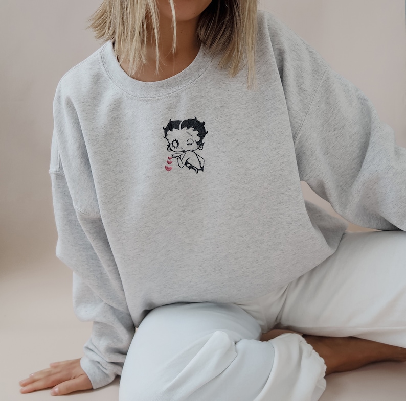 May include: A gray sweatshirt with a cartoon image of Betty Boop blowing a kiss with three pink hearts.