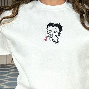 May include: White sweatshirt with a black embroidered image of Betty Boop blowing a kiss with three red hearts.
