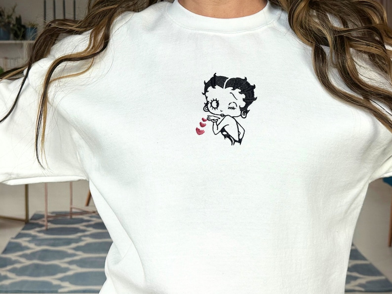 May include: White sweatshirt with a black embroidered image of Betty Boop blowing a kiss with three red hearts.