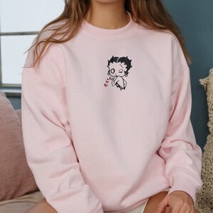 May include: A pink sweatshirt with a cartoon character of Betty Boop blowing a kiss with hearts around her.