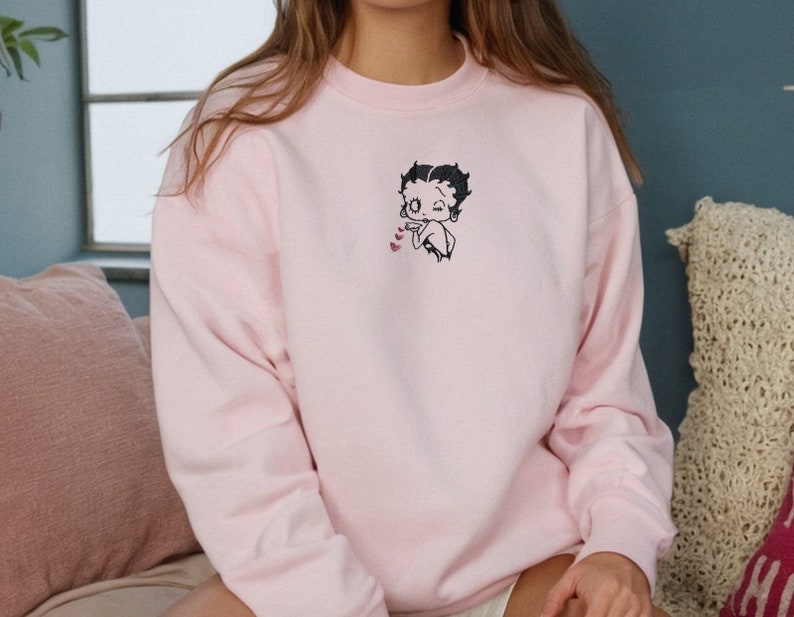 May include: A pink sweatshirt with a cartoon character of Betty Boop blowing a kiss with hearts around her.