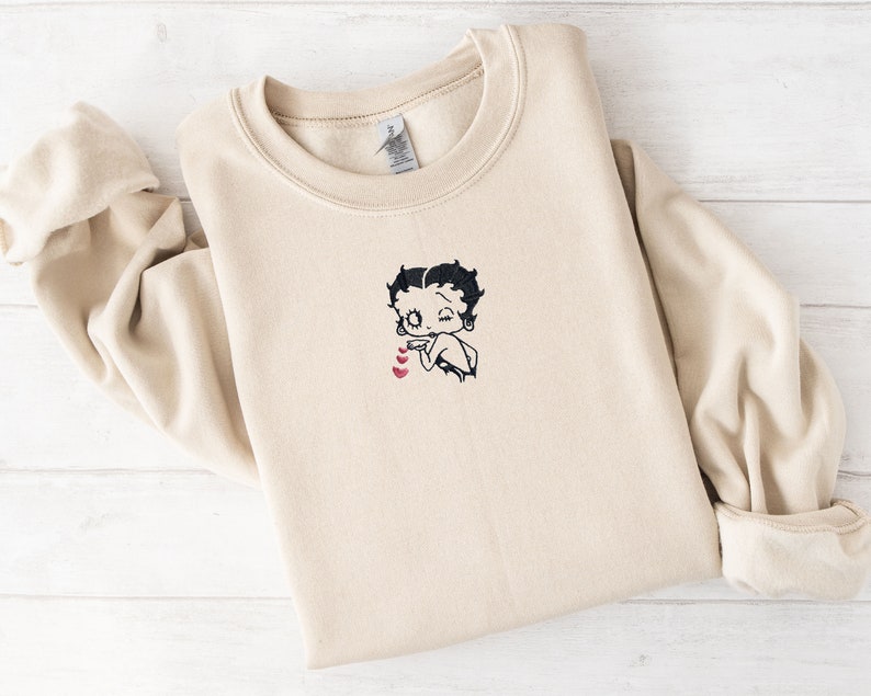 May include: A beige sweatshirt with an embroidered image of Betty Boop with hearts.