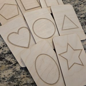 May include: Set of eight wooden cards with different shapes cut out: a heart, a star, a circle, an oval, a square, a rectangle, a triangle, and a pentagon.