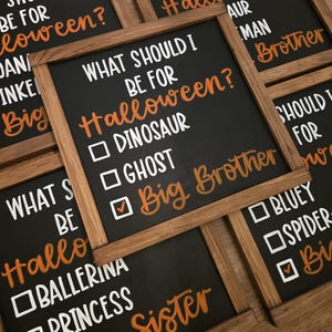 May include: Several small black chalkboards with wooden frames are arranged on a wooden surface. Each board has the question "What should I be for Halloween?" written in white and orange lettering, with check boxes for costume ideas.