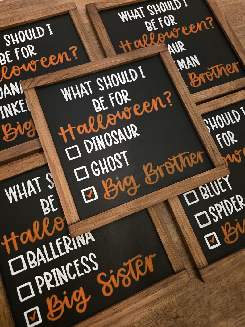 May include: Several small black chalkboards with wooden frames are arranged on a wooden surface. Each board has the question "What should I be for Halloween?" written in white and orange lettering, with check boxes for costume ideas.