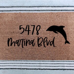 May include: A brown coir doormat with the address "5478 Martina Blvd." and a black silhouette of a dolphin jumping out of the water.