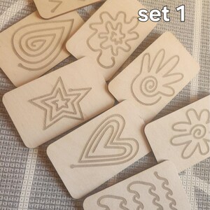 May include: Set of eight wooden tracing cards with various designs, including a star, heart, flower, hand, and wavy lines. The cards are labeled "set 1".