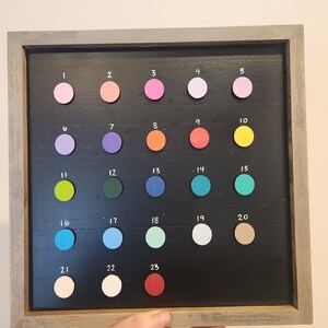 May include: A framed chalkboard with 23 numbered circles, each filled with a different color paint chip. The colors include pink, purple, orange, yellow, green, blue, red, and white.