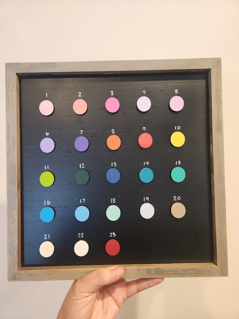 May include: A framed chalkboard with 23 numbered circles, each filled with a different color paint chip. The colors include pink, purple, orange, yellow, green, blue, red, and white.