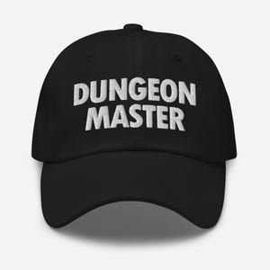 May include: A black baseball cap featuring the words DUNGEON MASTER embroidered in white capital letters across the front panel. The cap has a structured crown, a curved brim, and eyelets for ventilation on the top panels of the hat.