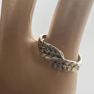 May include: A silver ring featuring a leaf design. The ring is worn on a finger, showcasing the intricate details of the leaf's texture. The ring's band is smooth and polished, contrasting with the textured leaf.