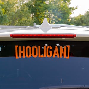 May include: A white car with a rear window sticker that says "[HOOLIGAN]" in orange letters.