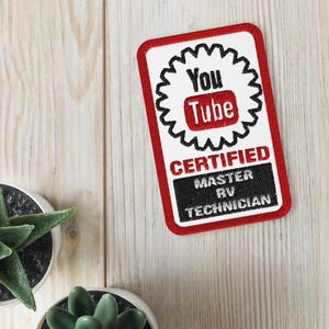 Puede incluir: Un parche rectangular con borde rojo y el logotipo de YouTube. El parche dice "You Tube CERTIFIED MASTER RV TECHNICIAN" en letras negras y rojas. El parche está sobre una superficie de madera clara.