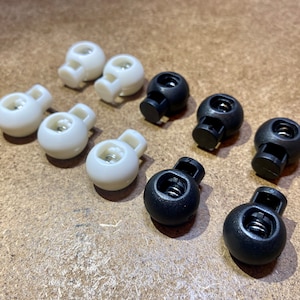 May include: A close-up of eight toggle clasps, four white and four black. The clasps are round and have a spring-loaded mechanism.