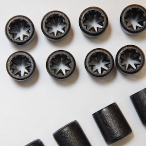 May include: A set of black plastic cord ends with a star-shaped hole in the centre. There are nine cord ends in total, with three additional cord ends that are solid black.