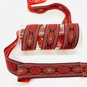 May include: Red and black patterned trim with a geometric design. The trim is rolled up on a clear glass cylinder.