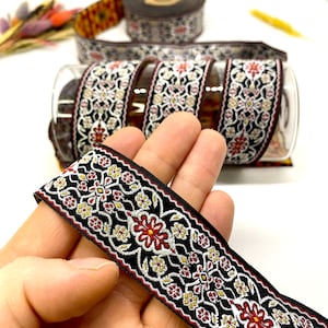 Puede incluir: Borde negro y blanco con bordado floral rojo y dorado. El borde está tejido y tiene una textura ligeramente en relieve.