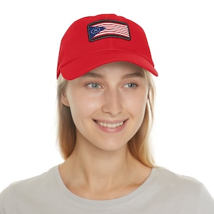 May include: A red baseball cap with a black and white patch featuring a flag with stars and stripes. The flag has a circle with a star in the center.
