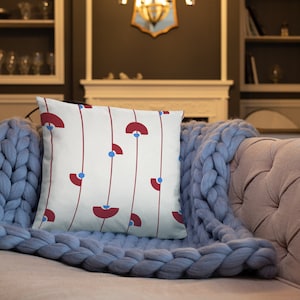 May include: A white throw pillow with a geometric pattern of red and blue shapes. The pillow is on a blue knitted throw blanket.