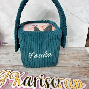 Può includere: Borsa a forma di scatola in velluto a coste color verde acqua con manico abbinato. La borsa ha il nome "Louka" ricamato in corsivo bianco. La parte superiore della borsa ha un motivo floreale. Un cartello dorato e rosa con la scritta "Kariscrp" è in primo piano.