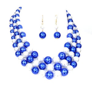 May include: A three-strand pearl necklace and matching earrings. The necklace is made of white and blue faux pearls. The earrings are blue.