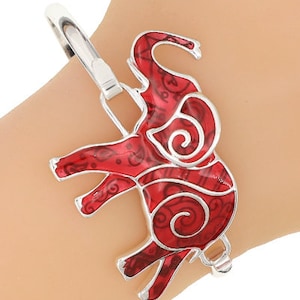 May include: A silver bracelet with a red enamel elephant charm. The elephant has intricate details and a swirling pattern.
