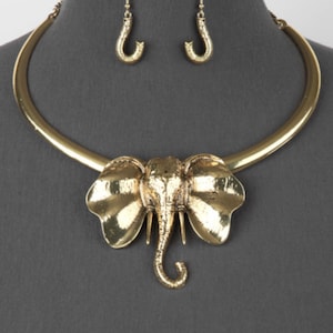 May include: Gold-tone elephant pendant necklace and matching earrings. The necklace features a wide, curved collar with a large elephant charm. The earrings are simple and dangle.