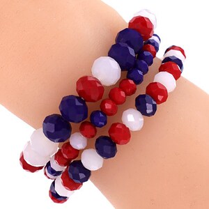 May include: A stack of three bracelets made of red, white, and blue beads. The bracelets are made of faceted glass beads.