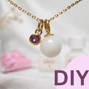 Puede incluir: Un collar dorado con dos colgantes. Uno es una pequeña gema redonda y morada. El otro es una perla esférica blanca. La palabra "DIY" es visible en la esquina inferior derecha.