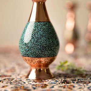 May include: A copper vase with a turquoise mosaic design on the body. The vase has a flared base and a narrow neck, with a polished copper finish. The vase is likely handmade and is a decorative item.