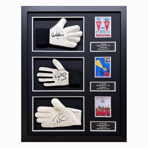May include: A framed display of three pairs of signed goalkeeper gloves, each with a small card featuring a player's information and a match ticket. The gloves are white with black accents and the signatures are in black ink. The cards are red, white, and blue.