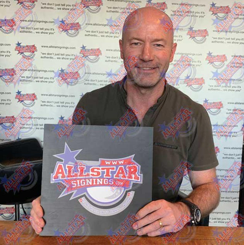 May include: A man holds a black square sign with a white logo that says "www.allstarsignings.com". The logo is red, white, and blue and features a star and a circle.