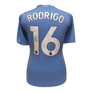 以下が含まれることがあります： 背面にRODRIGOという名前と16という数字が白でプリントされた、水色の半袖スポーツジャージ。襟元にはCITYという文字があり、数字の1の上には黒いサインと小さなリーグロゴが確認できます。