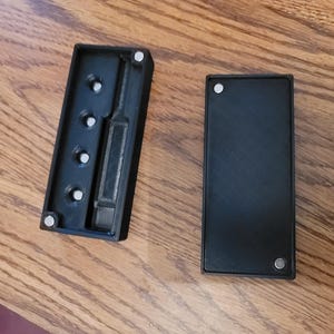 Puede incluir: Dos cajas de plástico negro con cierre magnético. Una caja tiene cinco pequeños agujeros redondos y una ranura rectangular. La otra caja es sólida.