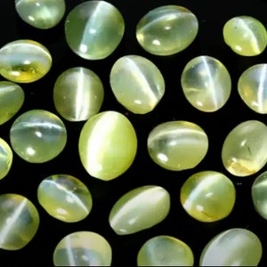 May include: A collection of oval-shaped green gemstones with a shimmering, iridescent effect. The stones have a light green color and a smooth, polished surface.