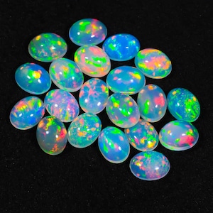 May include: A collection of oval-shaped opals with a vibrant play of color. The opals display a mix of blues, greens, pinks, and yellows, set against a translucent white base. The gemstones are arranged on a black surface.