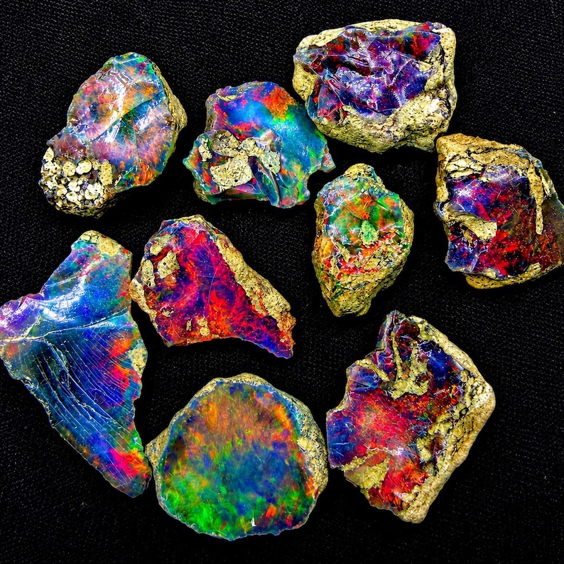 May include: A collection of nine raw, unpolished opal stones featuring vibrant flashes of red, blue, green, and purple iridescence. Each stone displays a unique, irregular shape with rough, textured edges and a mix of colorful, glossy surfaces.