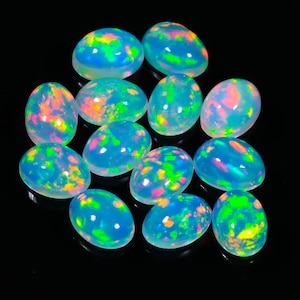 May include: A collection of oval-shaped opals with a translucent, milky blue base. Each stone displays vibrant internal color flashes of green, yellow, orange, and pink. The opals are arranged against a black background, highlighting their iridescent qualities.