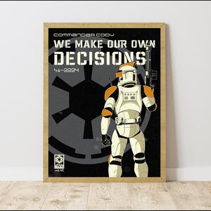 May include: Framed poster with a Star Wars theme, showing a clone trooper in white and orange armour, holding a blaster. The poster has the text "WE MAKE OUR OWN DECISIONS" and "Commander Cody" in white against a black background.