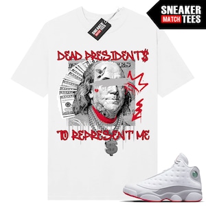 Könnte beinhalten: Weißes T-Shirt mit einer Grafik von Benjamin Franklin, Geldscheinen und dem Text "DEAD PRESIDENTS TO REPRESENT ME" in Rot. Ein Paar weiße und graue Turnschuhe mit roten Akzenten sind ebenfalls im Bild.
