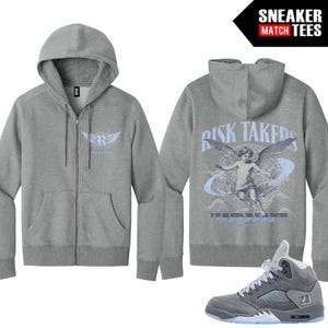 以下が含まれることがあります： グレーのジップアップパーカー。フロントポケットとフード付き。前面には「R」の文字と翼のロゴがあります。背面には「RISK TAKERS」の文字と「IF YOU RISK NOTHING, THEN YOU RISK EVERYTHING」のテキストが入った天使のグラフィックが表示されています。