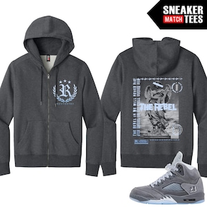 May include: Charcoal gray zip-up hoodie with a front logo and back graphic. The front features a light blue "R" logo with "Worldwide" text. The back displays an angel statue graphic with the text "The Rebel" and "The Rebel In We Will Never Die".