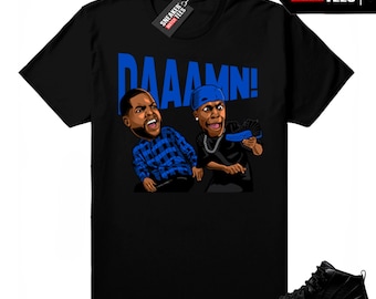 May include: Black t-shirt with a cartoon graphic of two men and the word "DAAAMN!" in blue. The graphic is paired with a black and blue sneaker. The shirt has a "Sneaker Match Tees" tag.