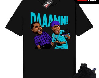 May include: Black t-shirt featuring a cartoon graphic of two men with the word "DAAAMN!" in teal. The graphic is paired with a black and purple Air Jordan 6 Retro sneaker. A tag with "SNEAKER MATCH TEES" is visible.