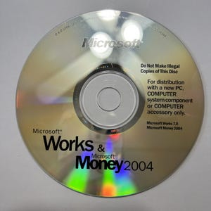 Peut inclure: Un CD-ROM argenté Microsoft Works & Money 2004. Le disque porte le logo Microsoft et le texte « Do Not Make Illegal Copies of This Disc ». Il indique également « For distribution with a new PC, COMPUTER system component or COMPUTER accessory only ».