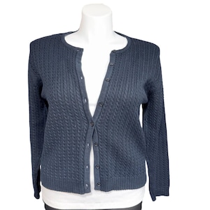 May include: A navy blue cable knit cardigan with a round neckline and button-up front. The long-sleeved sweater is displayed on a white mannequin. The cardigan is a classic style, suitable for layering.
