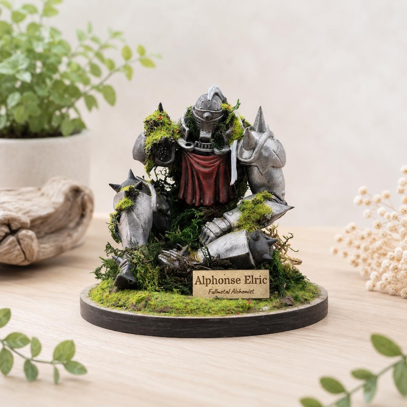 May include: A detailed figurine of Alphonse Elric from Fullmetal Alchemist, in silver armor, resting on a bed of green moss. A red cloth is visible at the chest. The figurine is on a round, black base with a small nameplate.