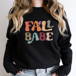May include: Black sweatshirt with a colorful graphic that says "Fall Babe" in a retro style.