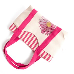 May include: A pink and white striped tote bag with a pink flower design. The bag has pink handles.
