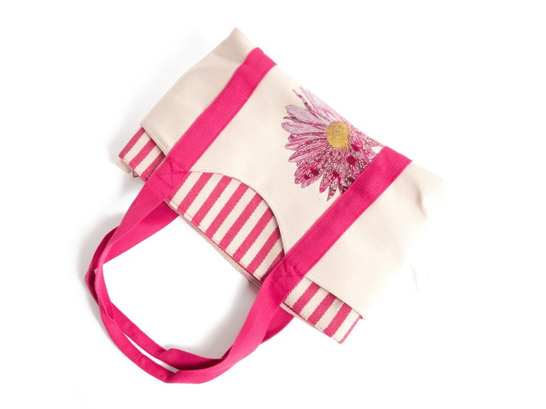 May include: A pink and white striped tote bag with a pink flower design. The bag has pink handles.